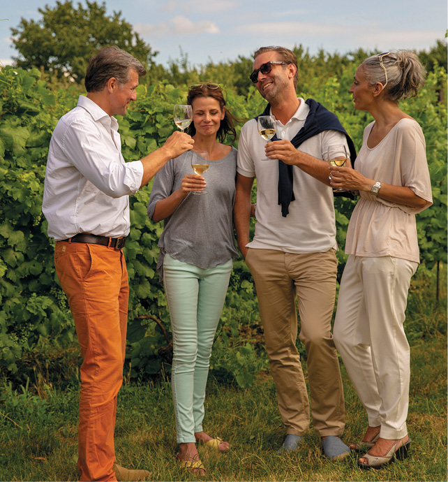 Four guests on a wine tasting excursion in a vineyard, smiling and sampling the locally made white wine