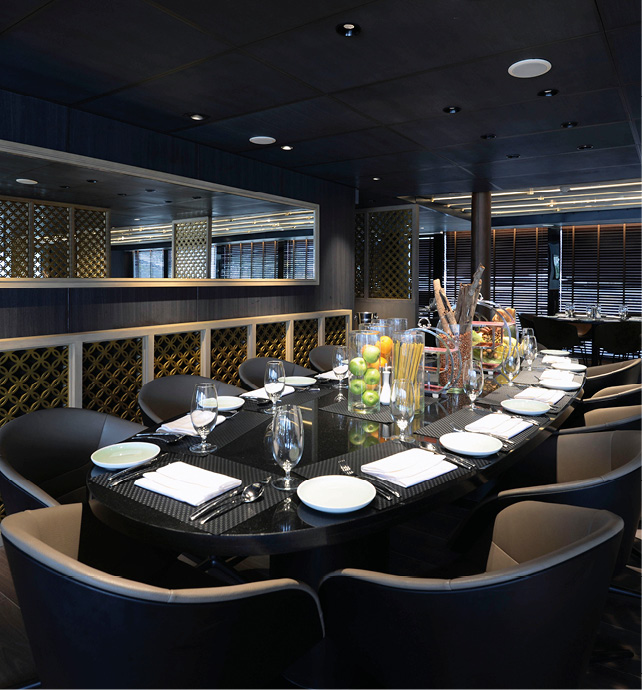 A large table complete with comfortable seating and dinnerware prepared for dinner on board Emerald Harmony’s Reflections Restaurant