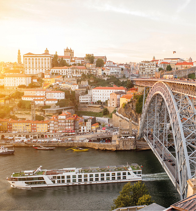 Luxury river ship sailing under a bridge in Porto at sunset