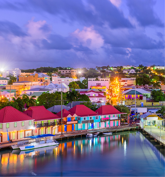 A cloudy St. John’s at dusk, with colourful buildings lit up, and waterfront buildings reflected in the sea